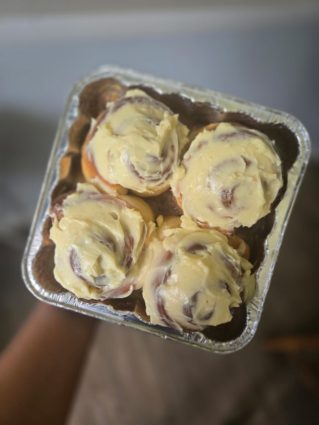 Four soft cinnamon rolls topped with cream cheese icing in a foil pan